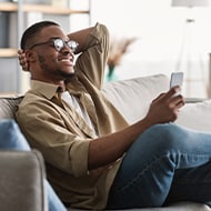 A man couple researchers LifeLock’s Million Dollar Protection Package on his phone while sitting on a sofa. 