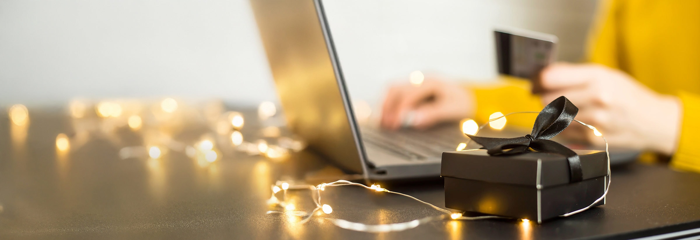 Person entering gift card details on a laptop with a small gift box nearby, illustrating Amazon gift card scams.