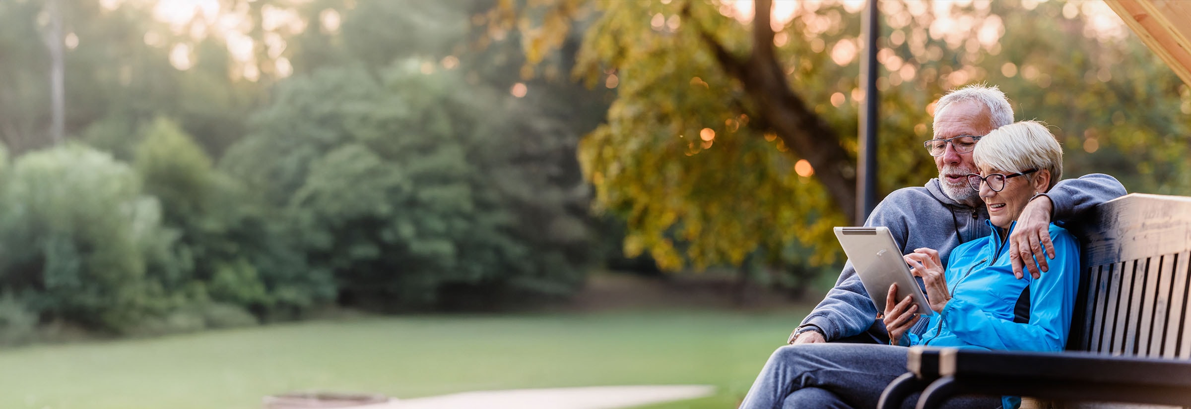 Two senior citizens sitting on a bench checking their identity theft protection service on a tablet.