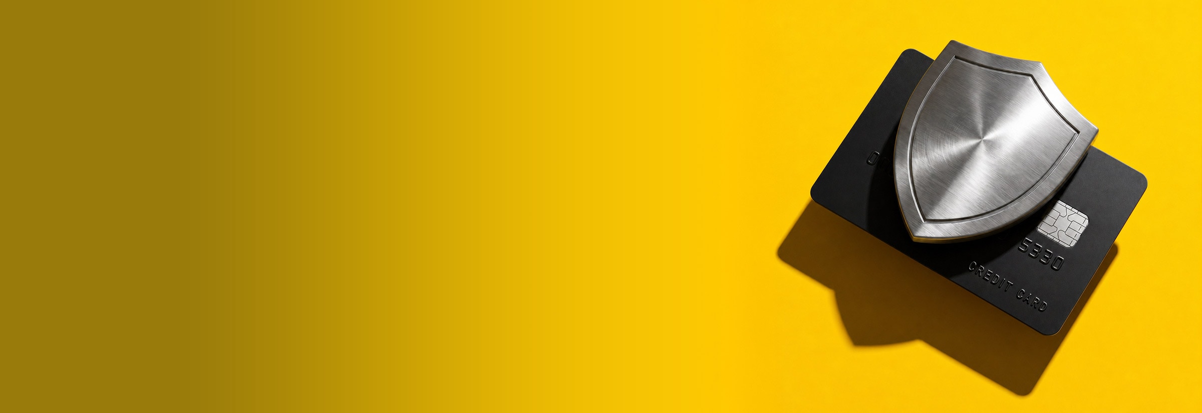 A top-down view of a brushed metal shield resting on a matte black credit card against a bright yellow background.