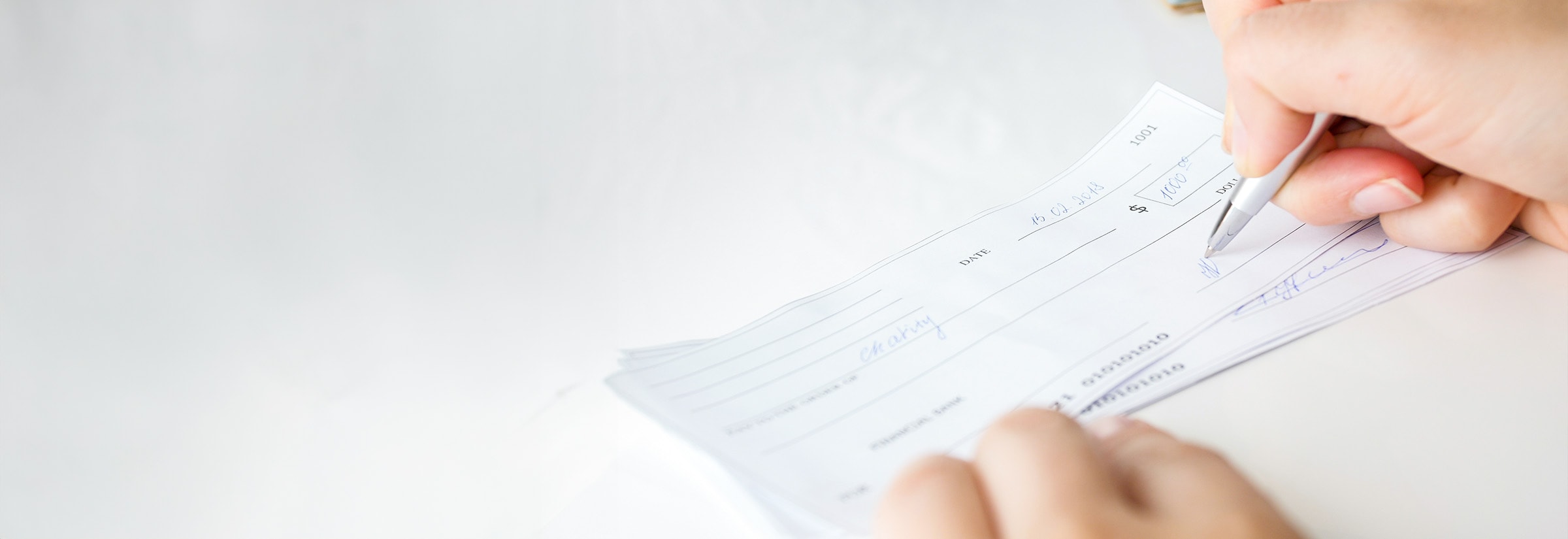 A person writing a check with the date to protect against check-date fraud.