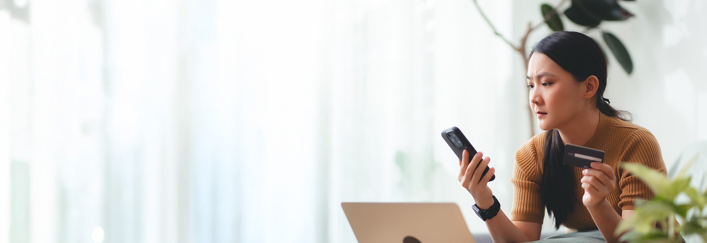Woman looking suspiciously at her smartphone while holding her credit card.