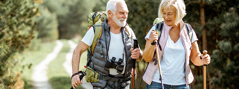 An active elderly man and woman hike on a trail.