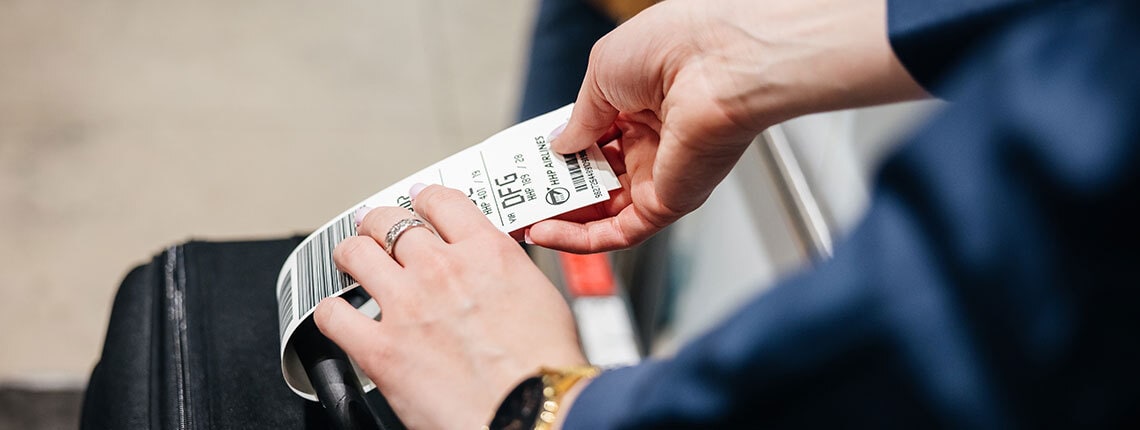 A hand holding an airline luggage tag attached to a suitcase.