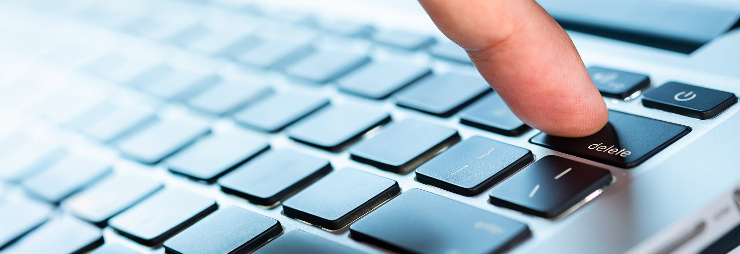 Finger pressing the “delete” key on a laptop.