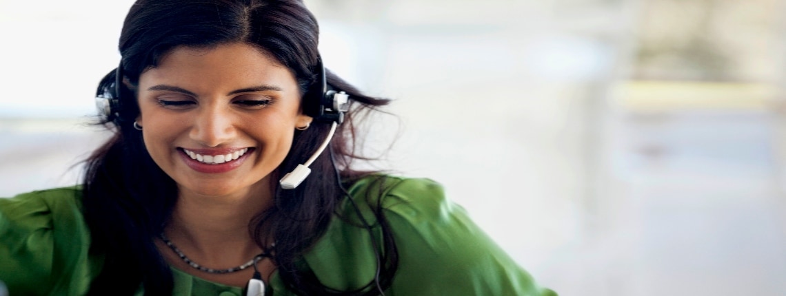 A woman in a green shirt wearing a headset and sitting at a computer.