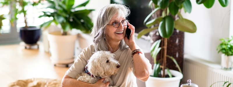 Woman taking happily on the phone with her white dog in hand.