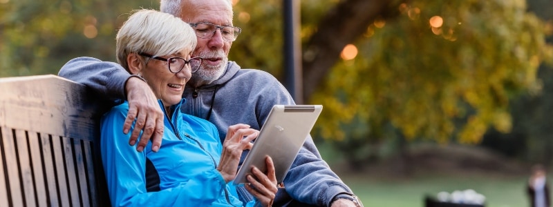 An older couple sitting on a bench learns about tax impersonation scams on their tablet.