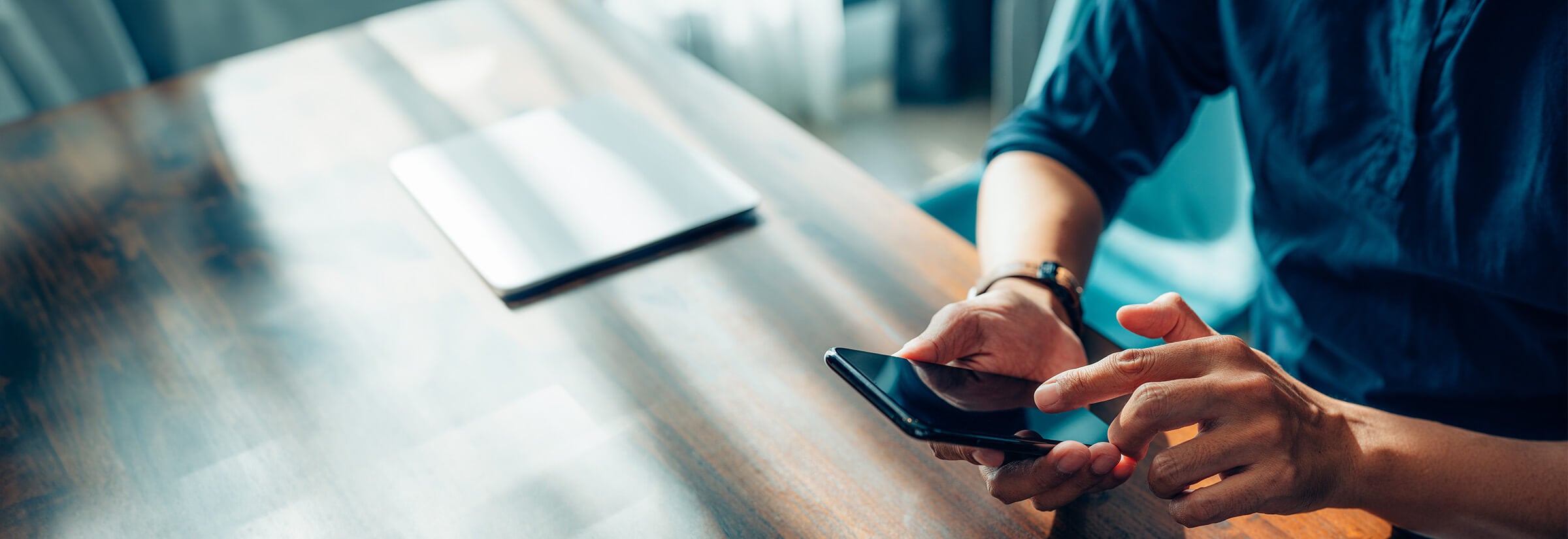 A man holding a phone, sitting at a table, next to a laptop.