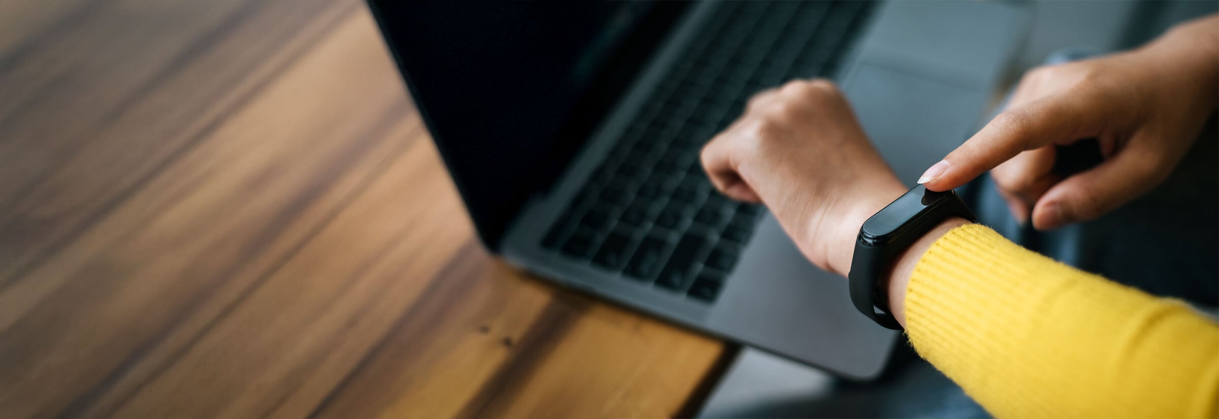 A person in a yellow sweater taps on their wearable device.