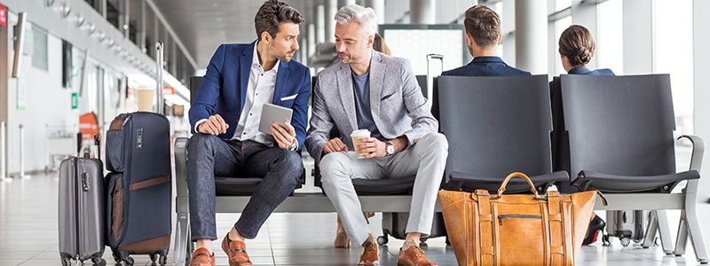 Two male travelers seated at an airport discuss what is personally identifiable information.
