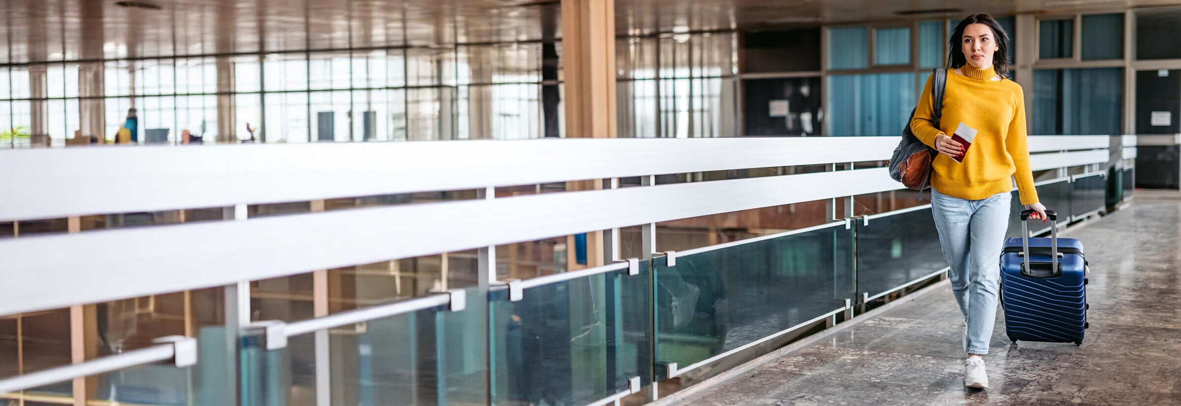 A woman walking through an airport with her passport in hand.