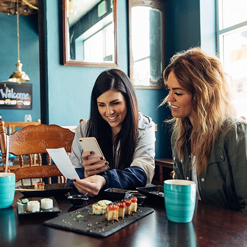 A woman on a city street checking that she isn’t falling for a Zelle scam on her phone.