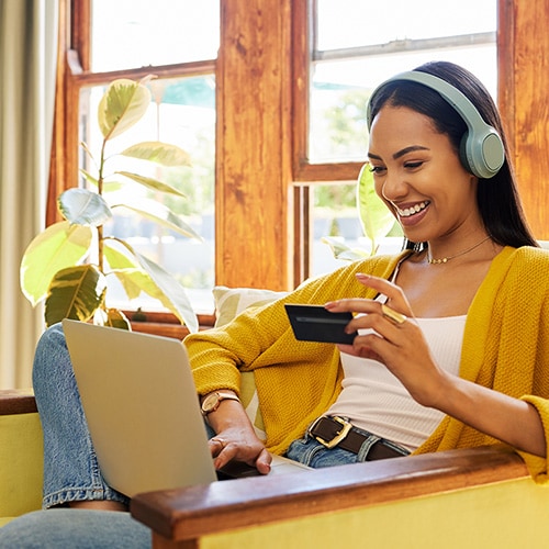 A woman sitting on a couch holding a mobile device and credit card.