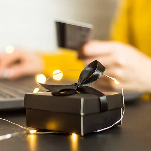 Person entering gift card details on a laptop with a small gift box nearby, illustrating Amazon gift card scams.