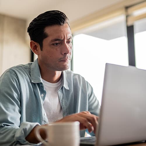 An Image of a man reading a Geek Squad scam email on his laptop.