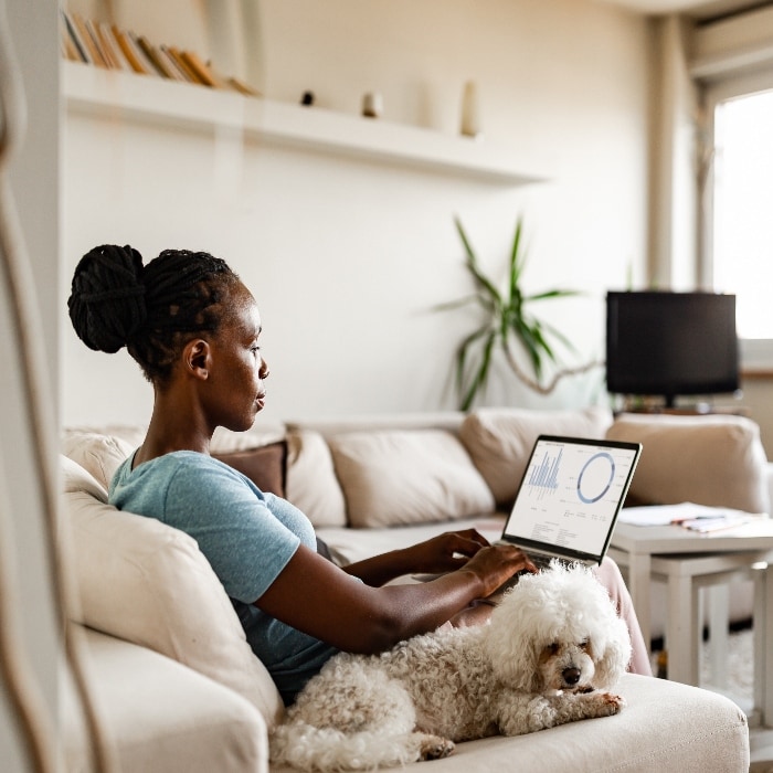 Image of a woman witting on a couch with a dog and her laptop.