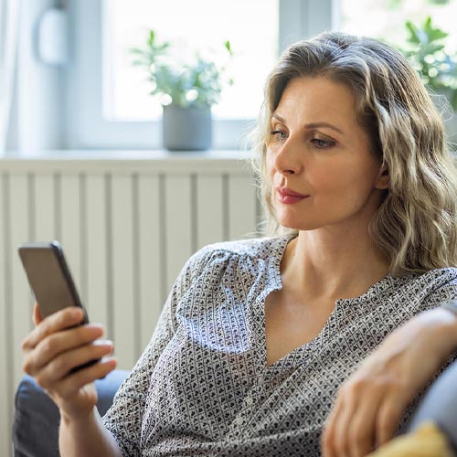 An image of a woman lounging and researching how to identify a fake text message.