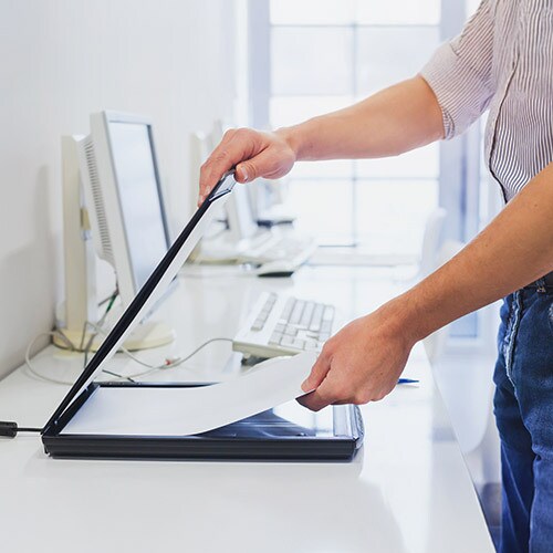 Person operating a scanner on an office desk, scanning sensitive documents safely.
