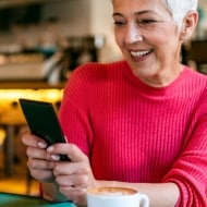A woman with short white hair sits in a café smiling at her phone.