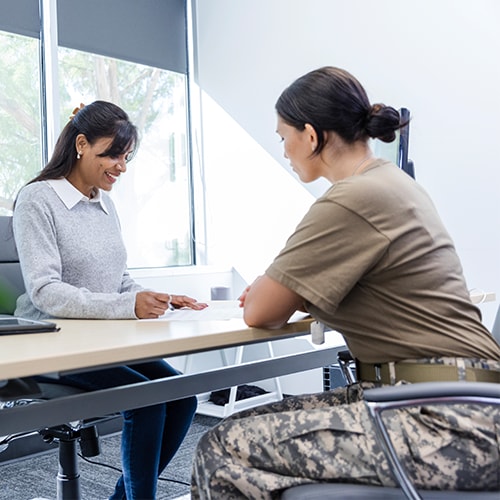 Two people sitting at a desk. One woman is dressed in military attire.