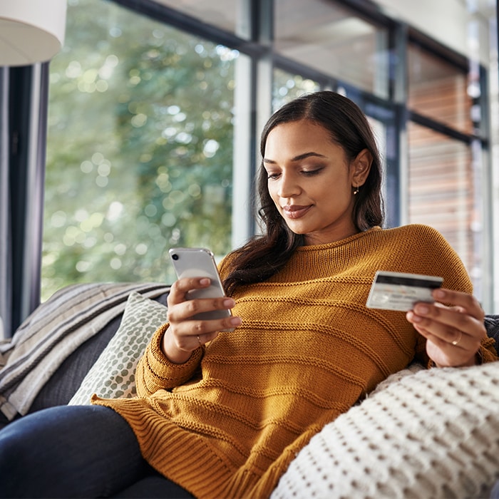 A woman sitting on a couch holding a mobile device and credit card.
