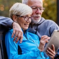 An older couple sitting on a bench learns about tax impersonation scams on their tablet.