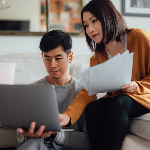 A young couple reviewing physical and digital copies of their credit reports.