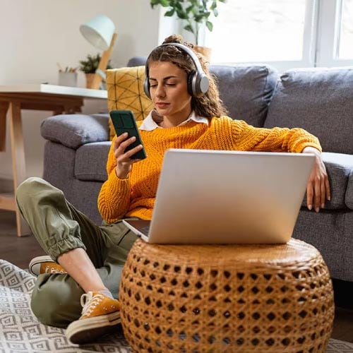 An image of a woman sitting in her living room checking a fraud alert on her phone.