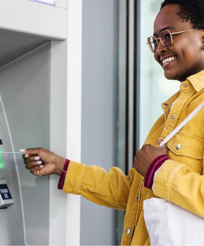 A smiling woman inserts her credit or debit card into an ATM after learning how to avoid wire transfer scams.